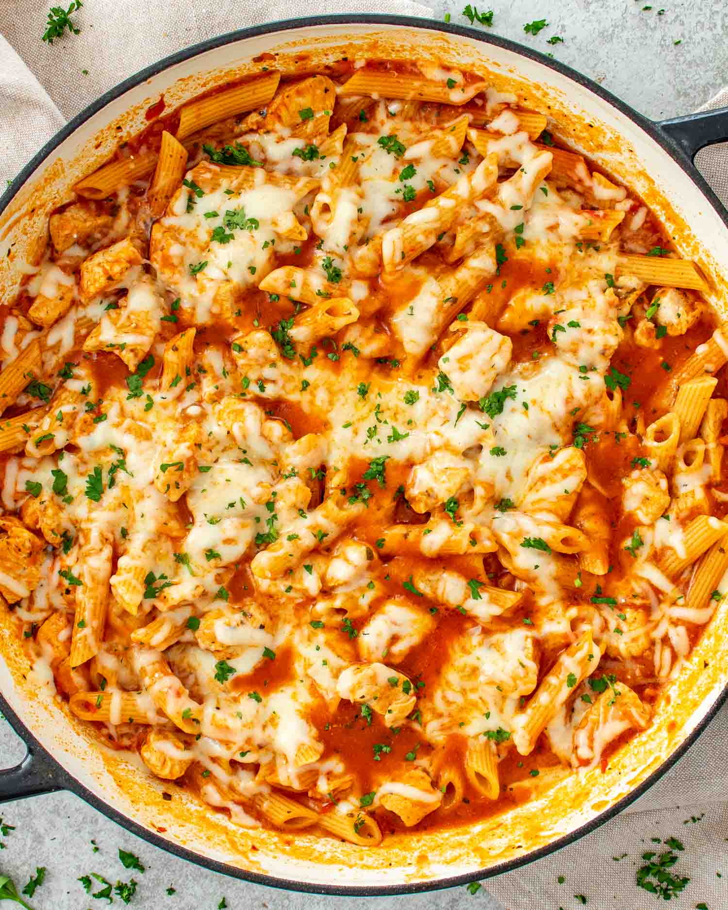 Easy chicken parmesan pasta skillet topped with melted mozzarella and parmesan cheese, garnished with parsley in large skillet.