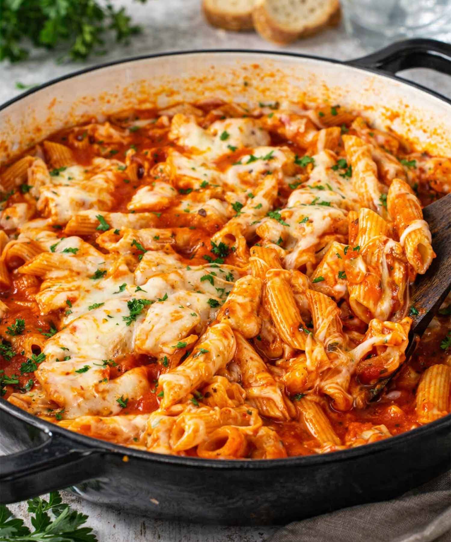 Chicken parmesan pasta skillet in large pan with penne, tender chicken, marinara sauce, and melted mozzarella being scooped with spoon.