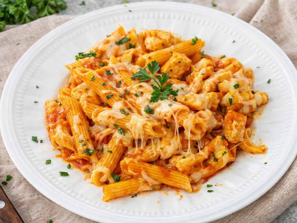 Serving of chicken parmesan pasta skillet on white plate with penne, juicy chicken, marinara sauce, melted cheese, and parsley garnish.