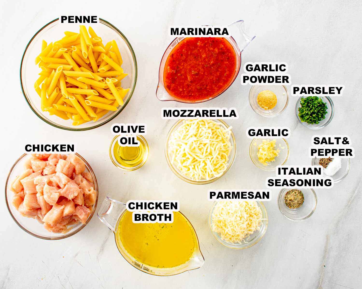 Ingredients for chicken parmesan pasta skillet including penne, chicken, marinara sauce, mozzarella, parmesan, garlic, olive oil, and seasonings arranged overhead.