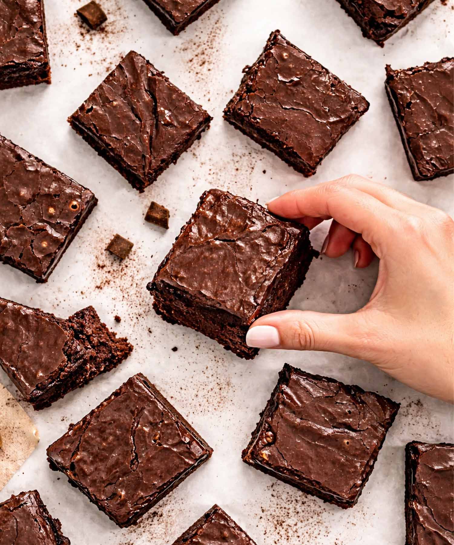 Overhead view of fudgy lunch lady brownies with glossy frosting, hand picking up square, rich chocolate crumb and crackly top visible.