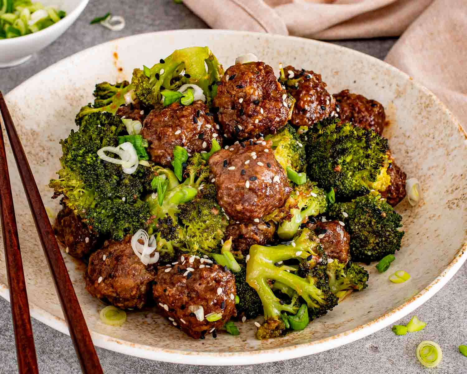 Healthy sheet pan dinner of glazed meatballs and broccoli garnished with green onions and toasted sesame seeds.
