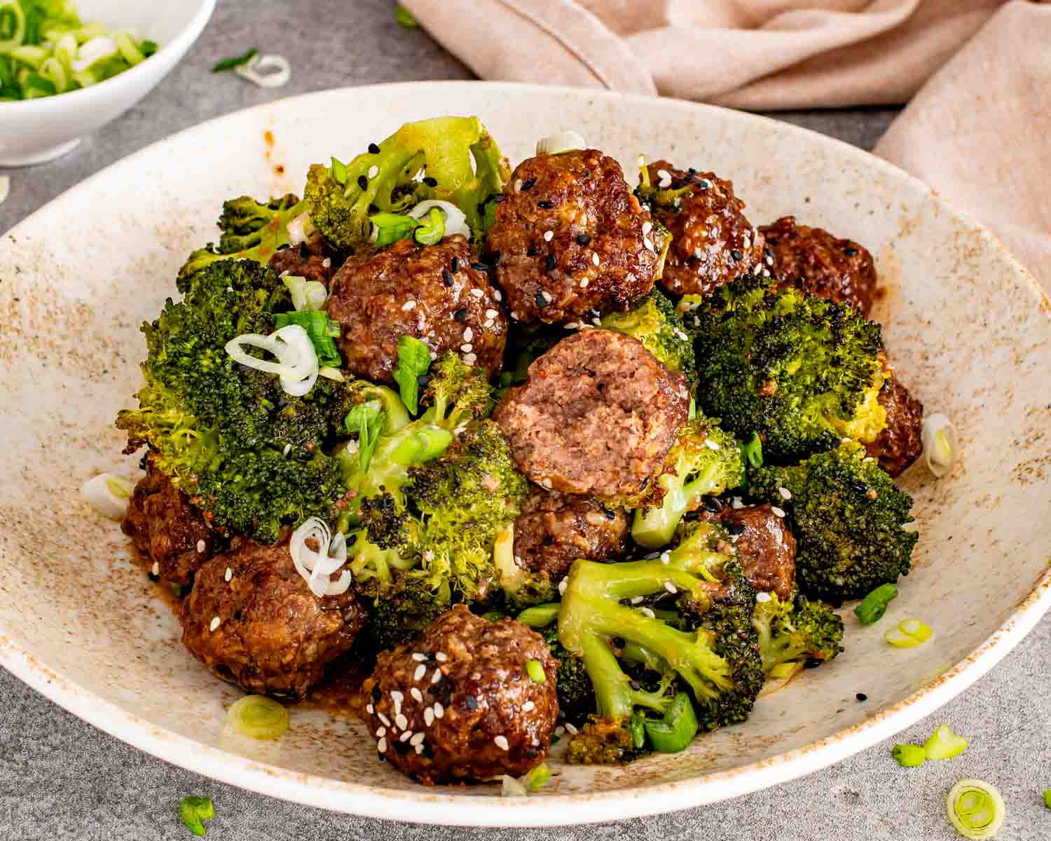 A honey garlic meatball sliced open to show juicy interior texture served with roasted broccoli florets.