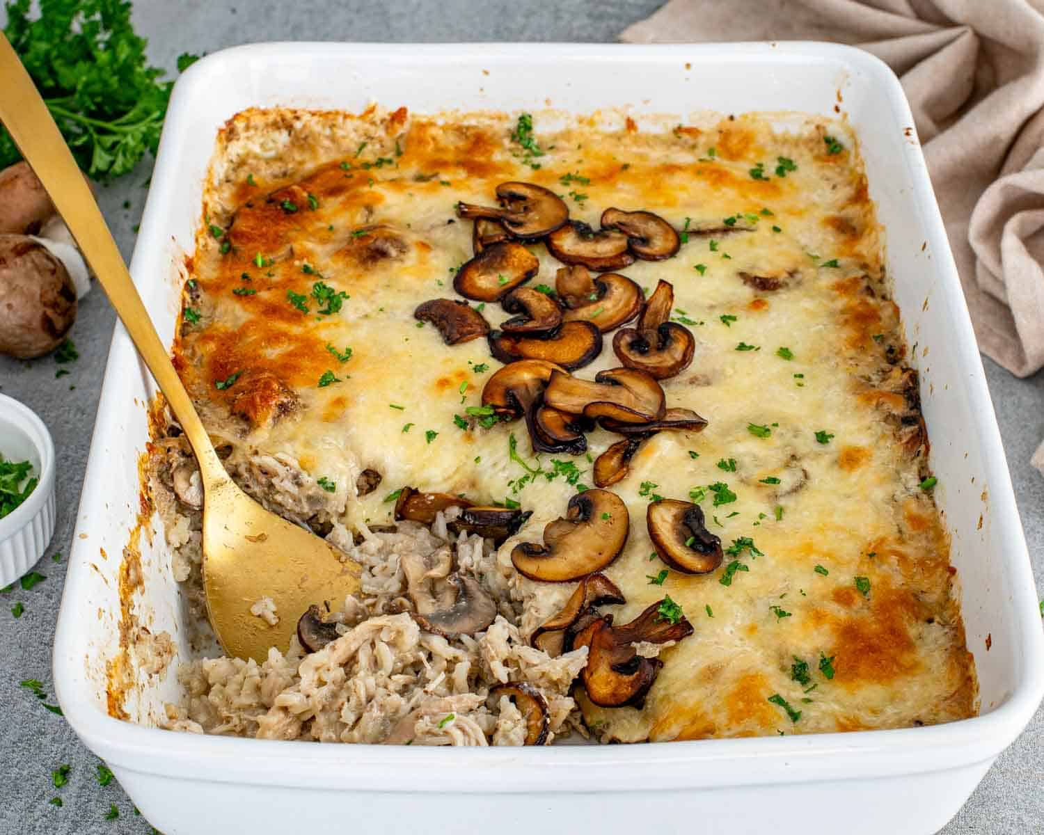 Spoon lifting chicken and mushroom rice casserole showing creamy rice, shredded chicken, melted cheese, and saut&eacute;ed mushrooms.