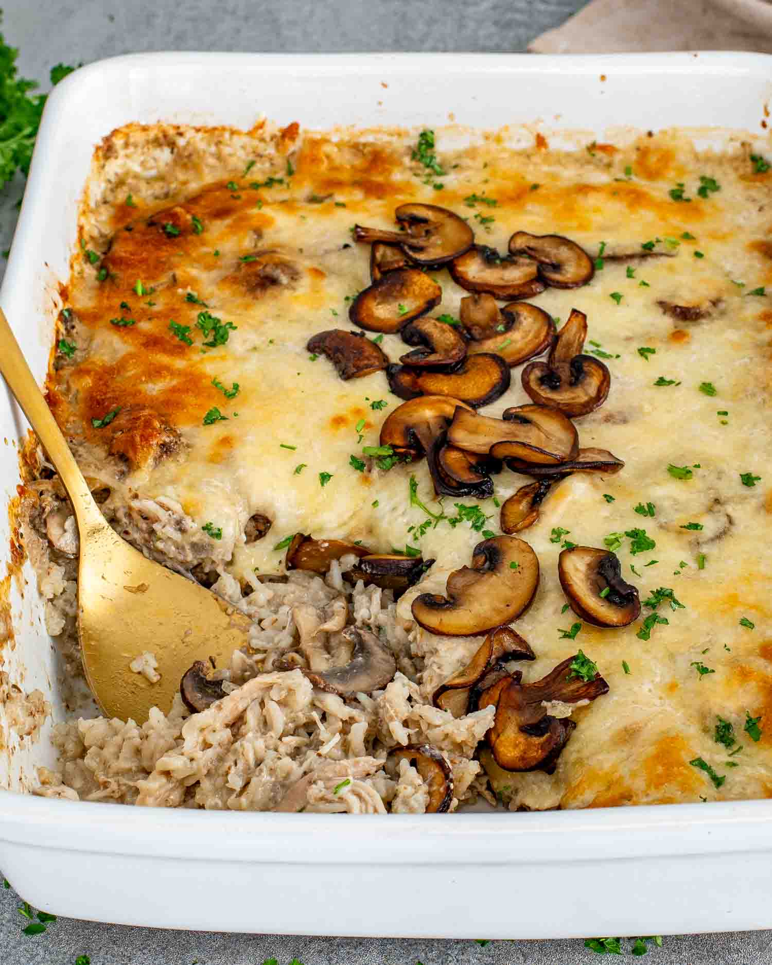 Chicken and mushroom rice bake in white casserole dish with melted cheese, golden top, and saut&eacute;ed mushrooms, creamy baked rice underneath.