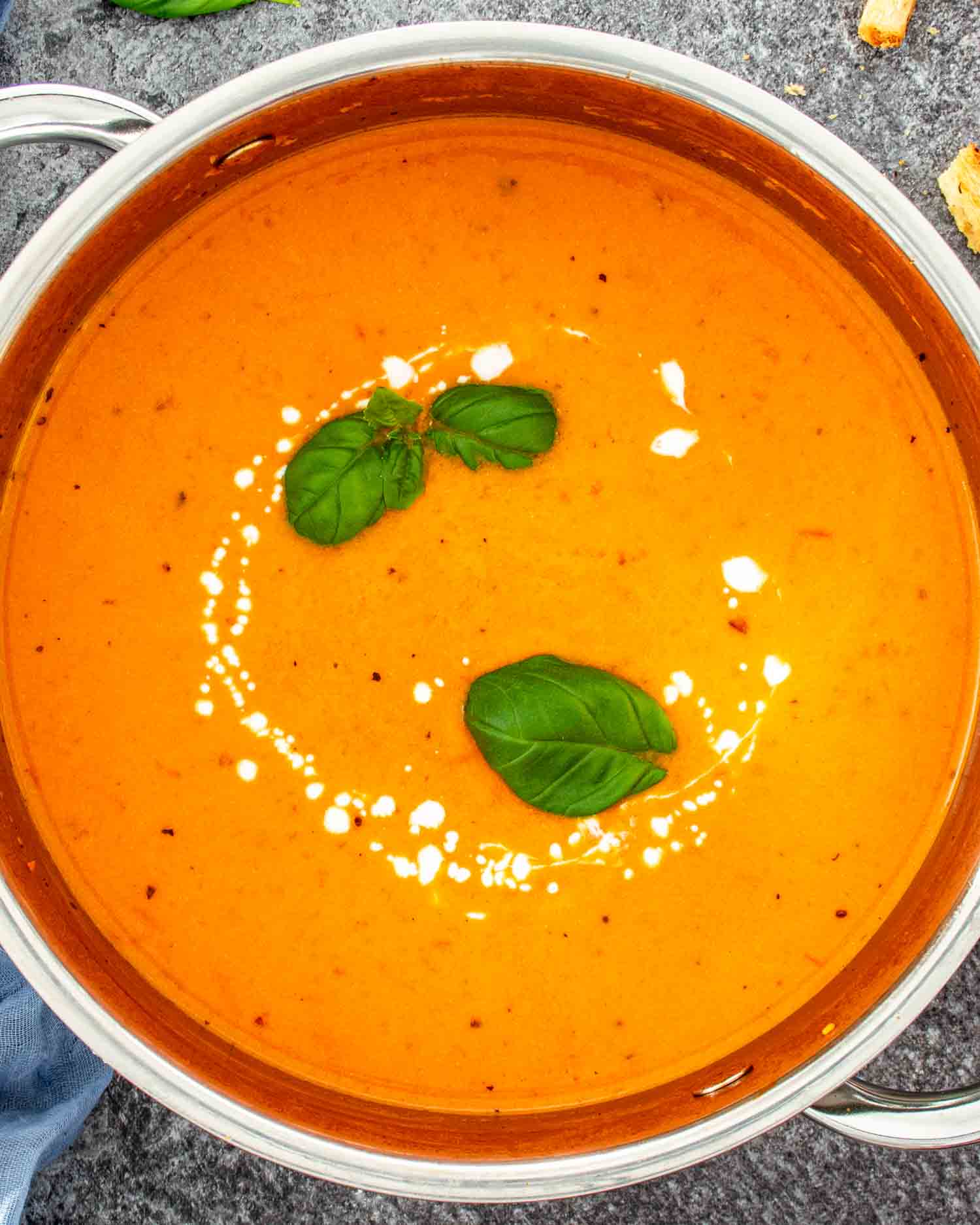 Overhead view of a large pot of creamy tomato soup with a cream swirl and fresh basil leaves garnished on top.