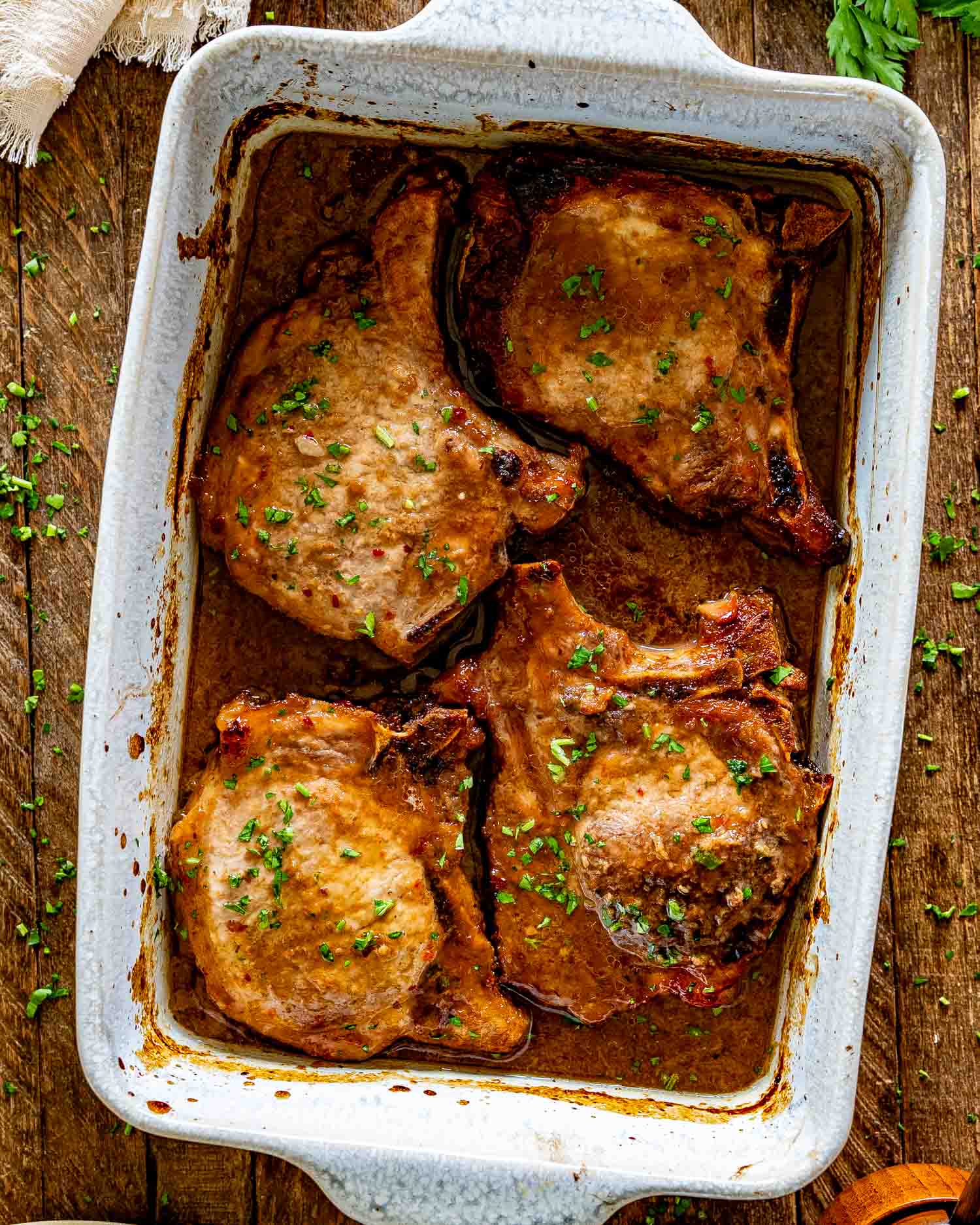Overhead view of baked brown sugar Italian pork chops nestled in savory sauce and sprinkled with fresh parsley.