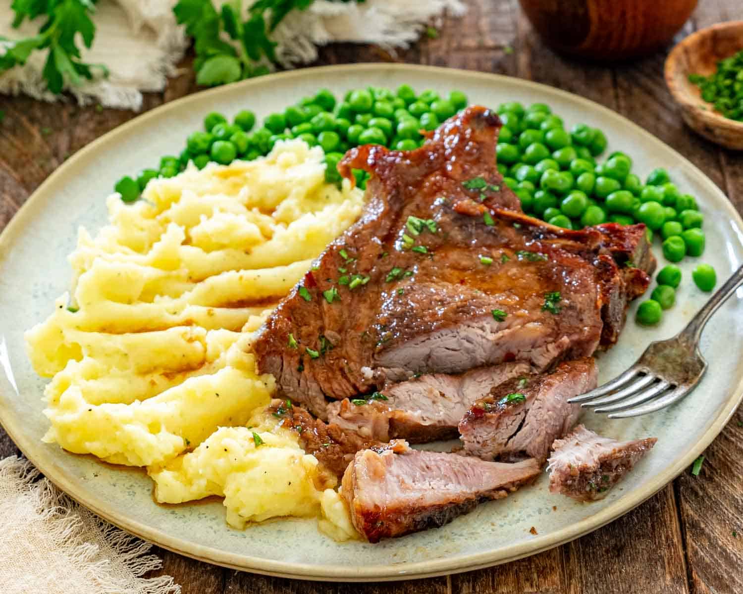 Tender brown sugar Italian pork chop sliced and served alongside buttery mashed potatoes and vibrant green peas.