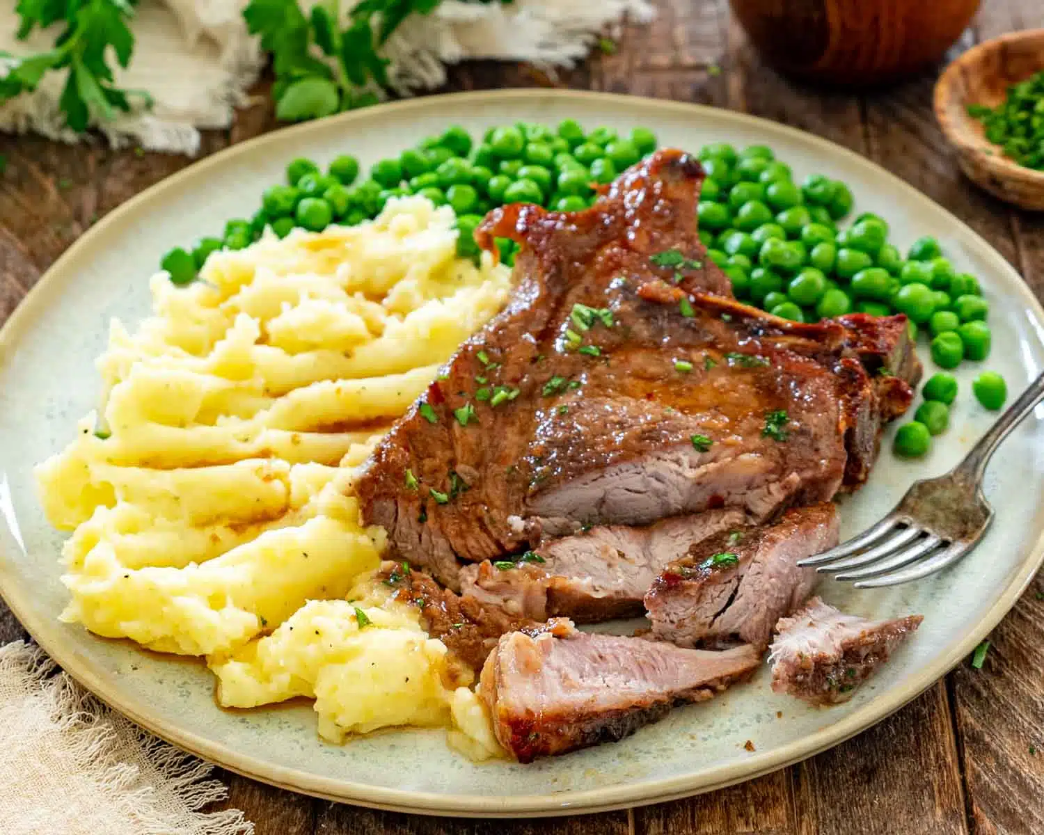 Tender brown sugar Italian pork chop sliced and served alongside buttery mashed potatoes and vibrant green peas.