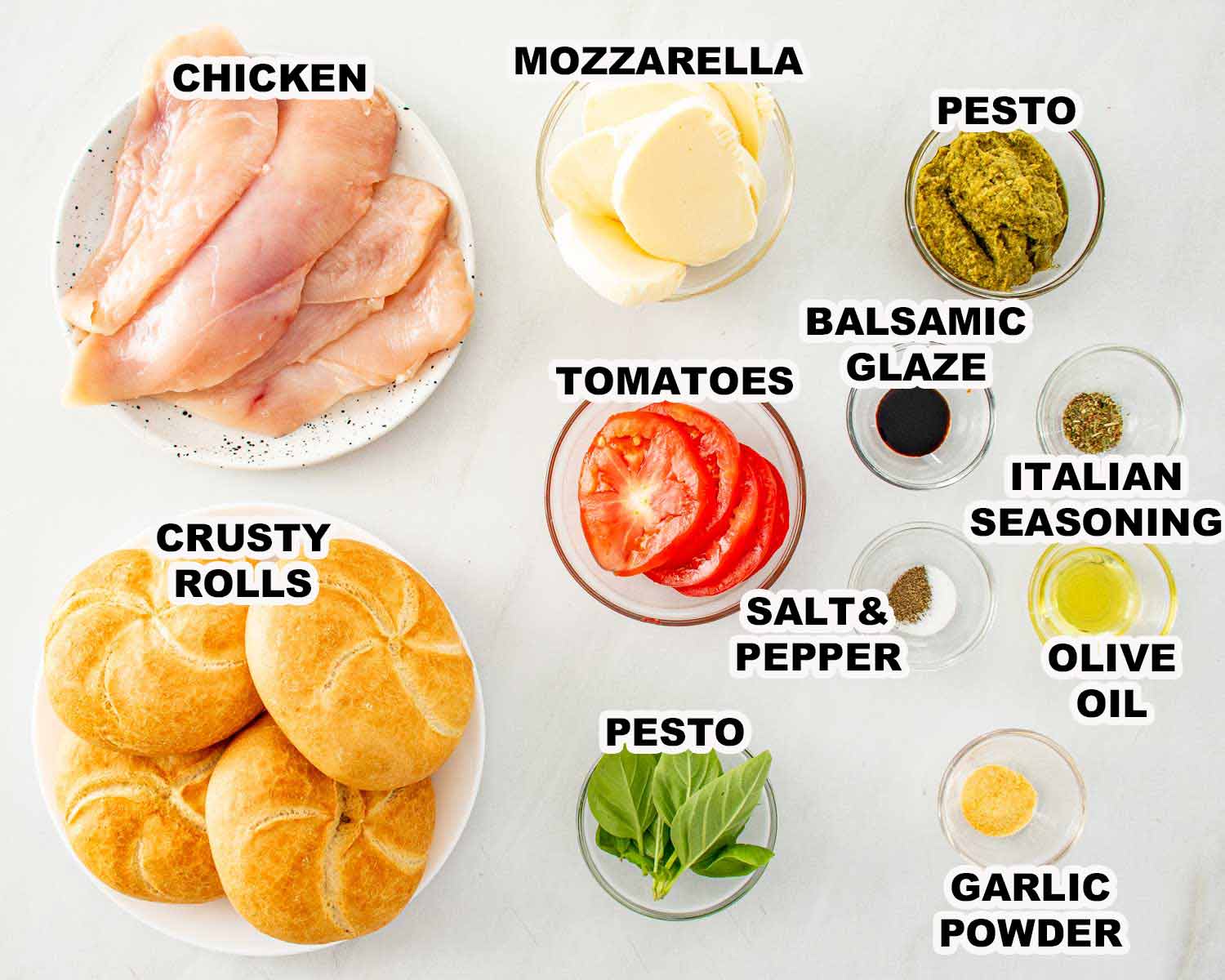 Ingredients for grilled chicken Caprese sandwiches including chicken, crusty rolls, mozzarella, tomatoes, basil, pesto, olive oil, and seasonings.