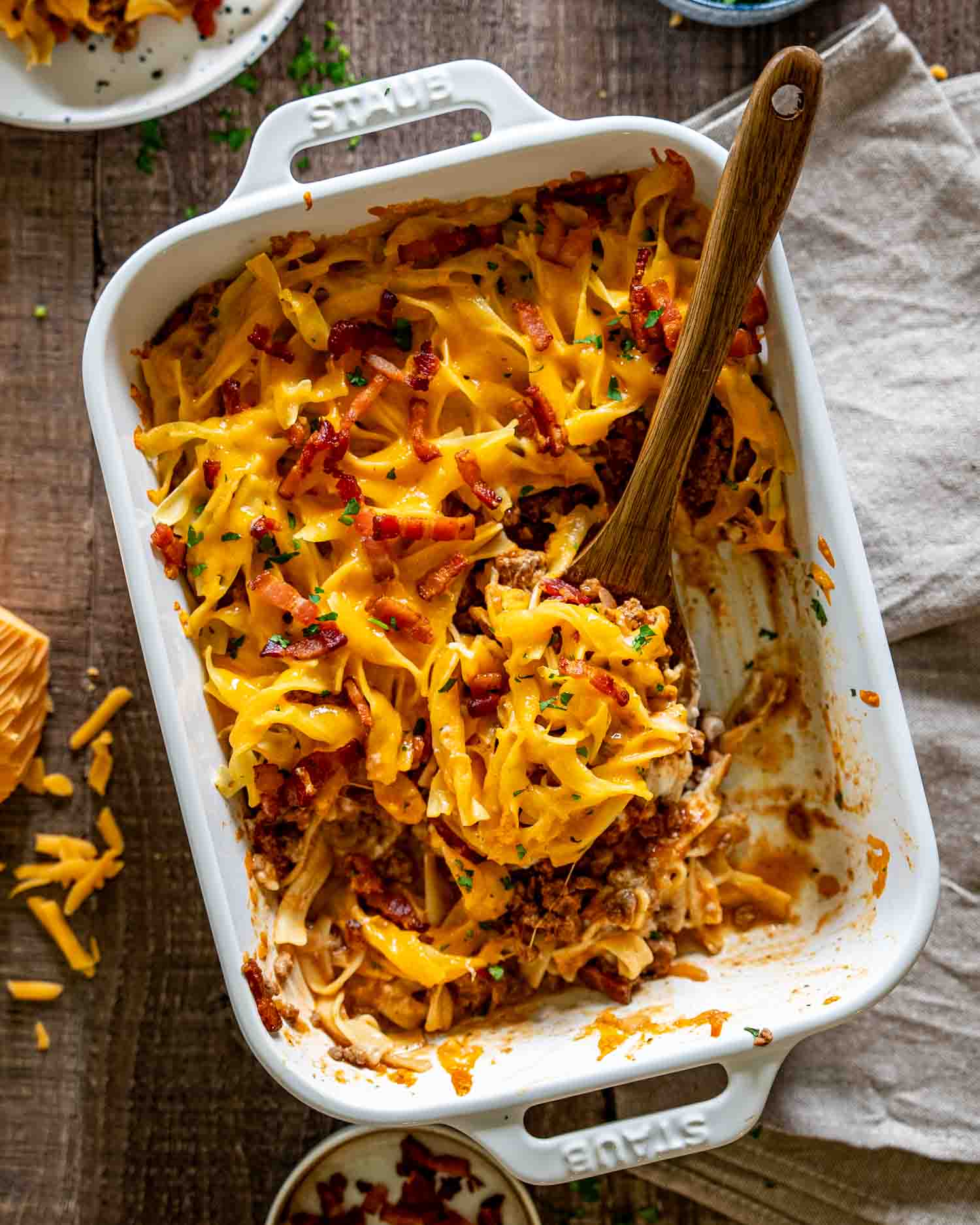 Overhead view of million dollar beef casserole in baking dish with serving spoon and rustic styling.