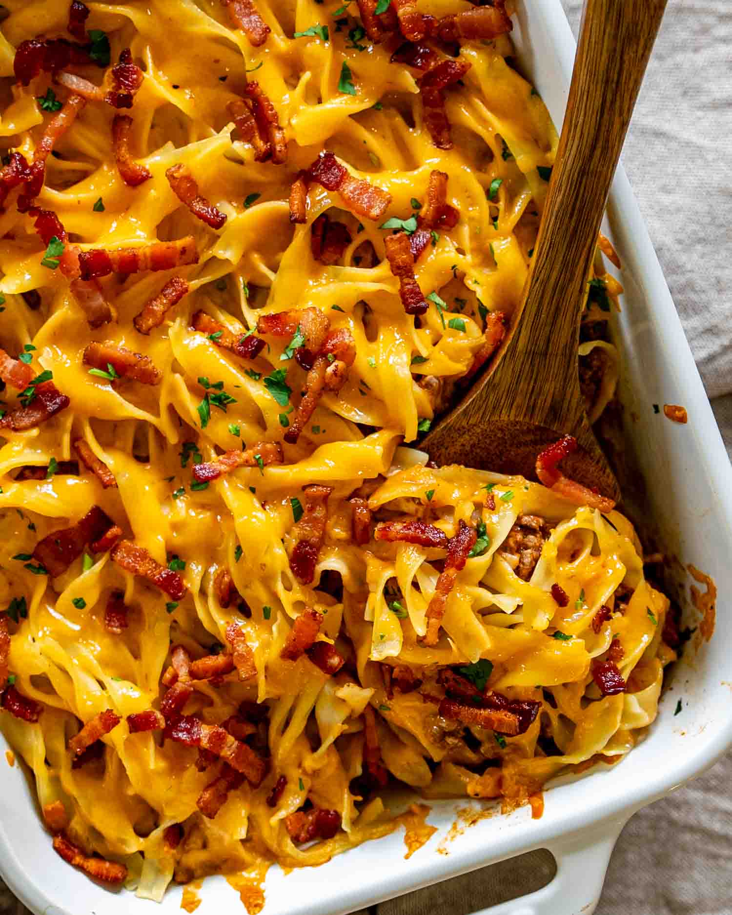 Close-up of baked casserole showing melted cheddar cheese, crispy bacon pieces, and tender egg noodles.