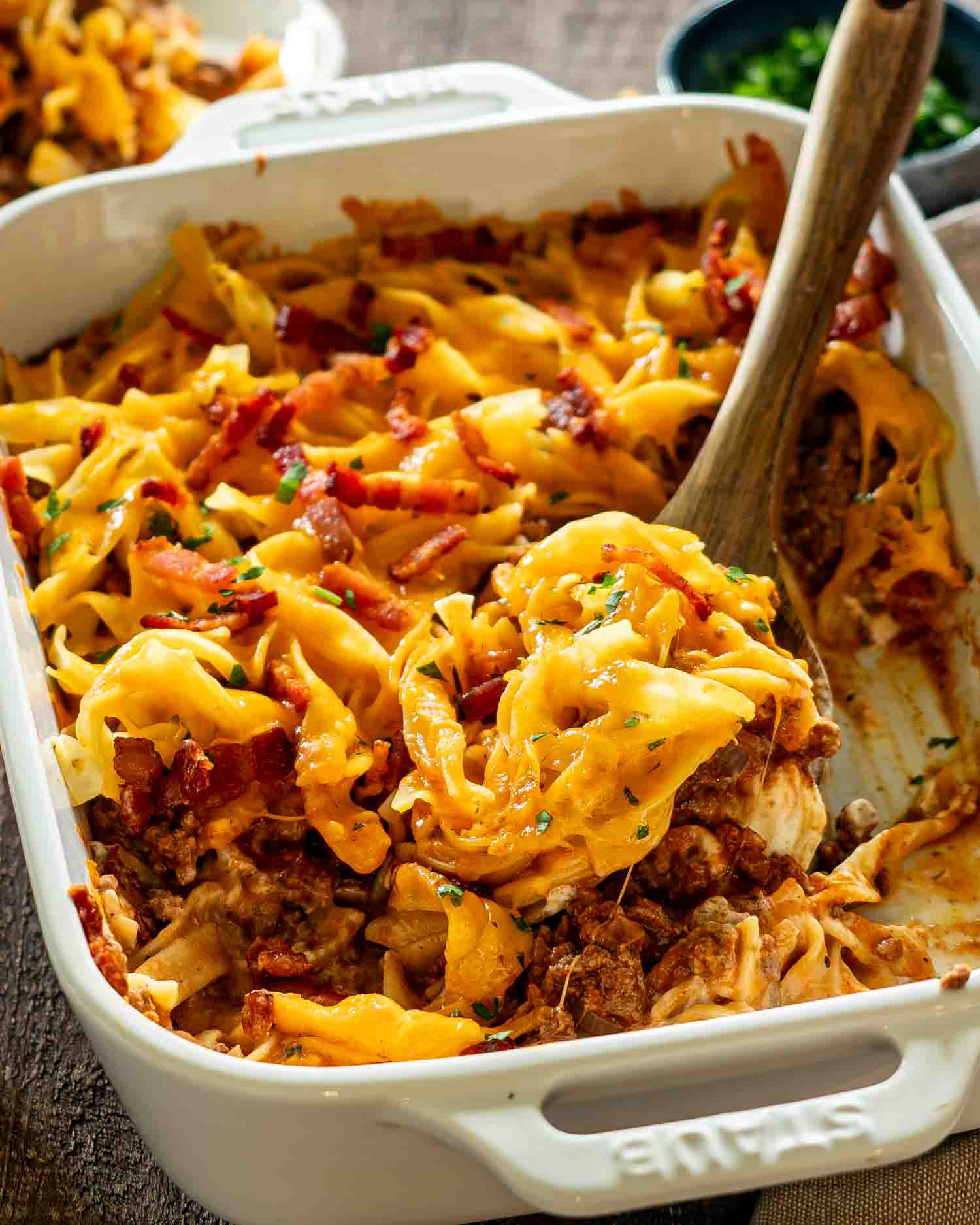Freshly baked beef casserole in white baking dish topped with melted cheddar cheese and crispy bacon.