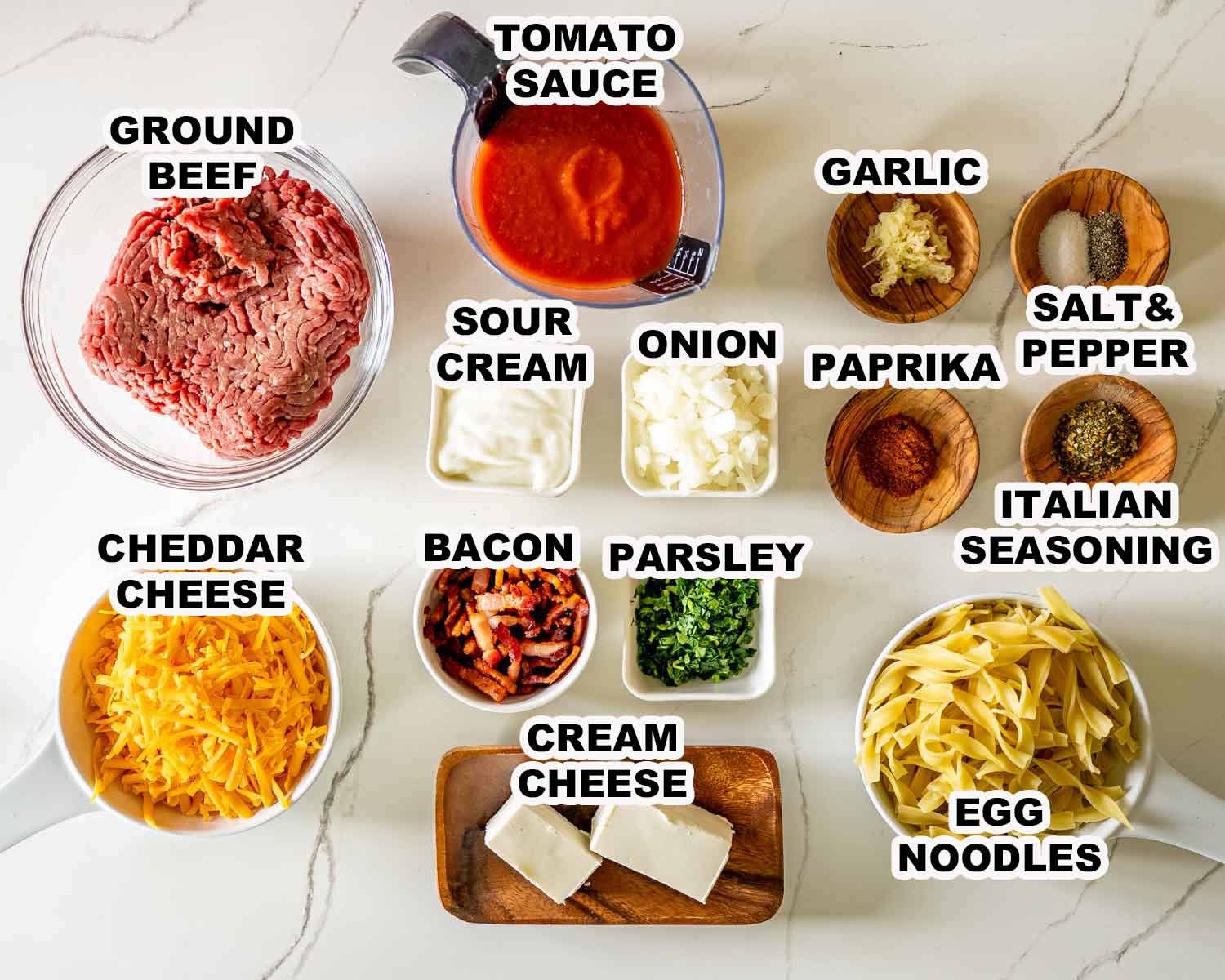 Ingredients for million dollar beef casserole including ground beef, noodles, cheeses, bacon, tomato sauce, and seasonings.