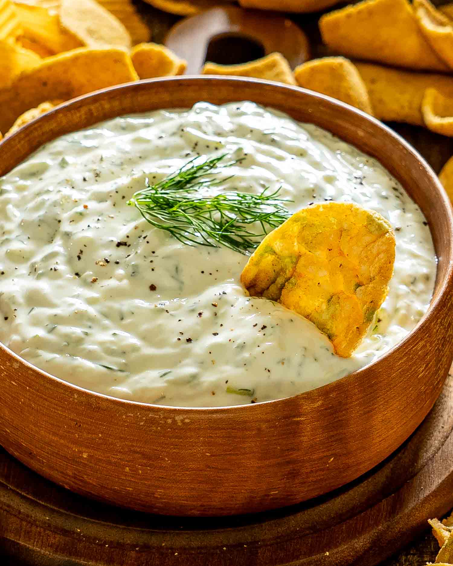 Creamy homemade tzatziki sauce topped with fresh dill and black pepper, served with a crisp chip for dipping.