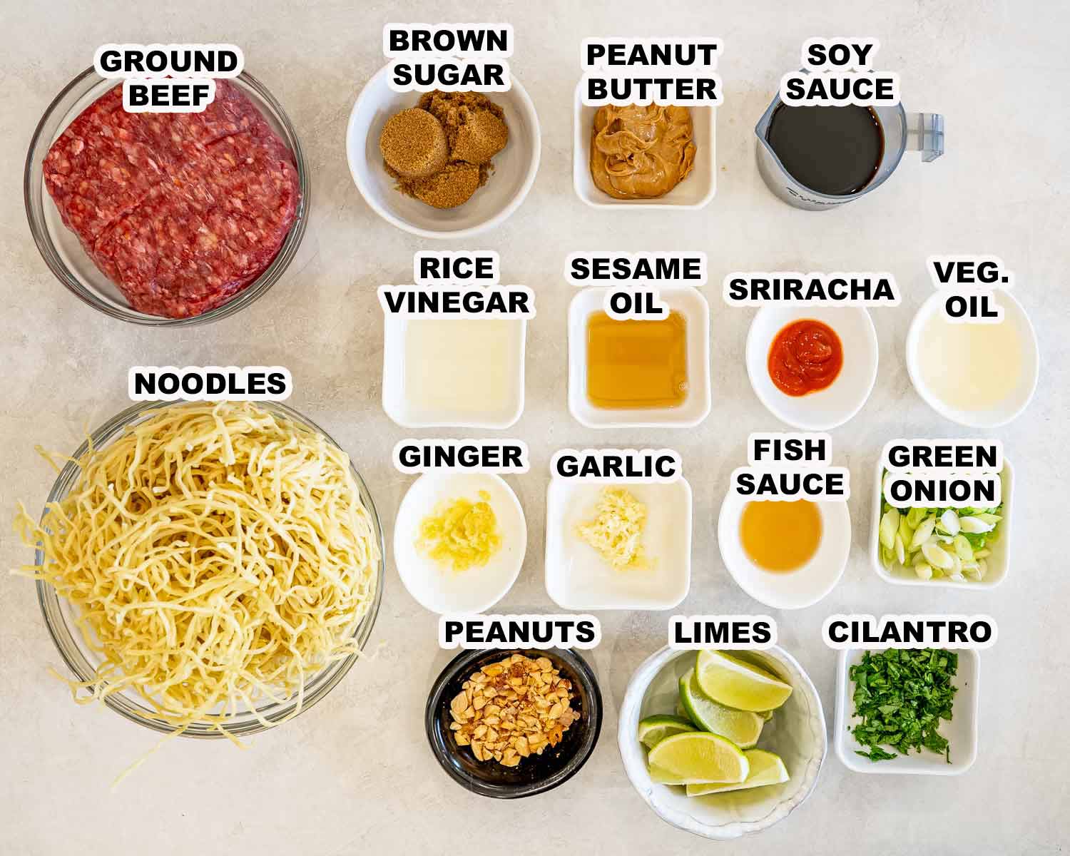 Overhead arrangement of labeled ingredients for caramelized beef and peanut noodles, including sauces, aromatics, garnishes, noodles, and ground beef.