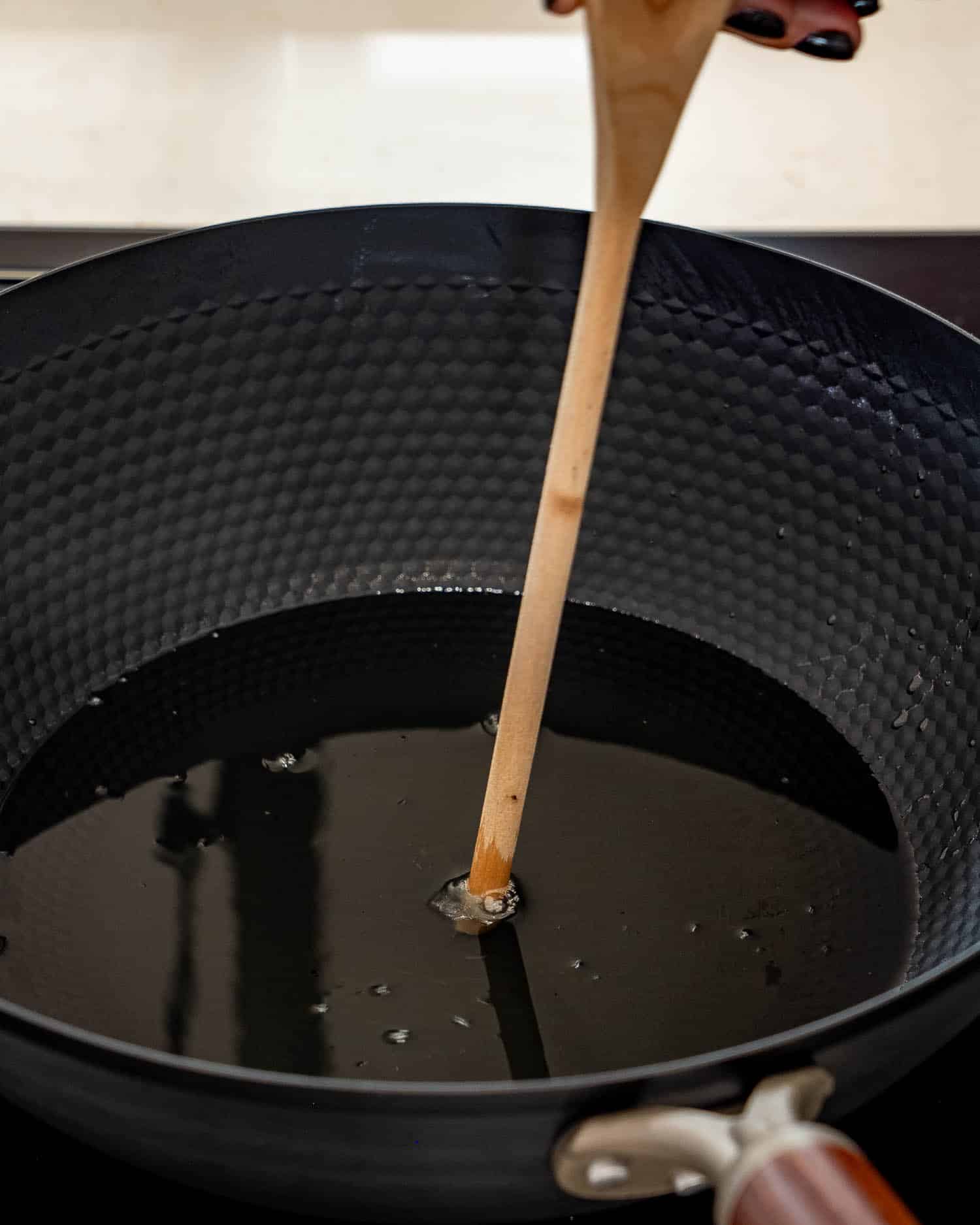 Wooden spoon handle dipped into hot oil shows bubbles forming around it, indicating the oil is ready for frying.