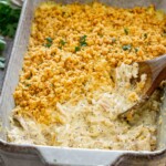 Close-up of creamy poppy seed chicken casserole with a golden cracker topping, fresh parsley, and wooden serving spoon.