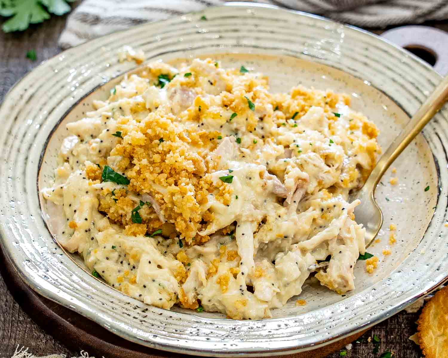 Creamy poppy seed chicken casserole topped with golden cracker crumbs and parsley is served in a rustic bowl.