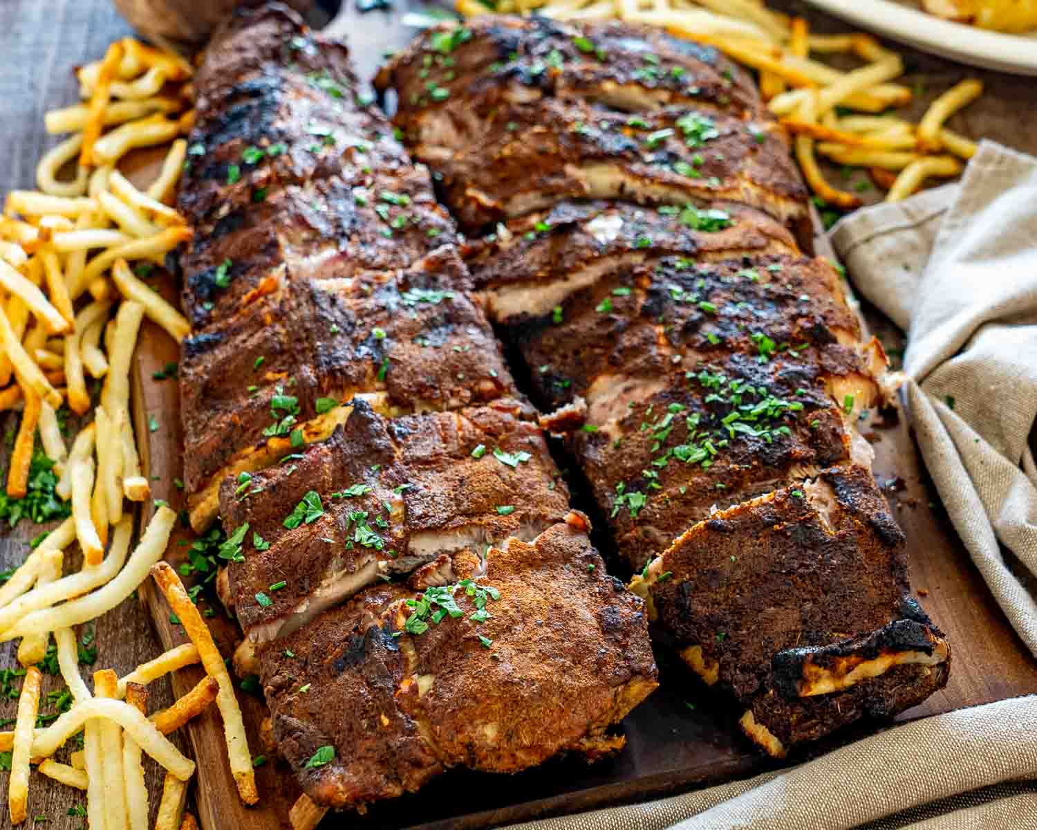 Two whole racks of Memphis-style pork ribs garnished with parsley and surrounded by golden fries.