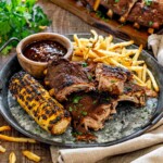 Memphis-style pork ribs served with grilled corn, crispy fries, barbecue sauce, and fresh parsley on a rustic platter.