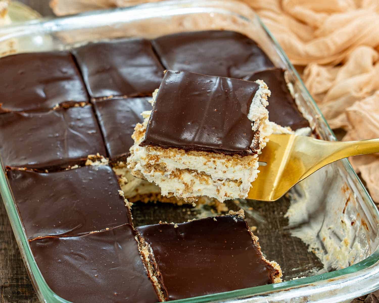 A square of creamy no bake chocolate eclair cake is lifted from neatly cut portions in a glass dish.