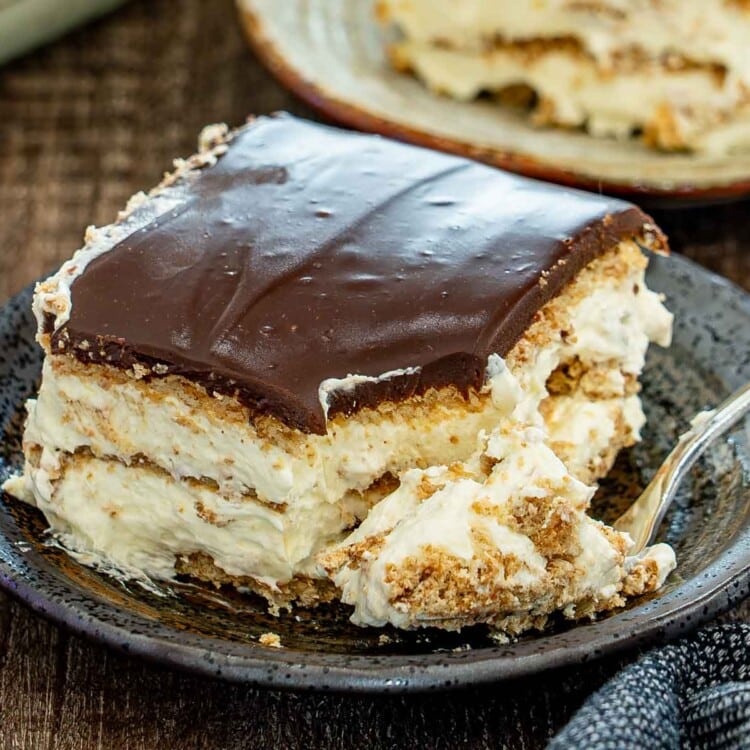 A partially eaten slice of creamy chocolate eclair cake shows soft graham cracker layers beneath glossy chocolate ganache.