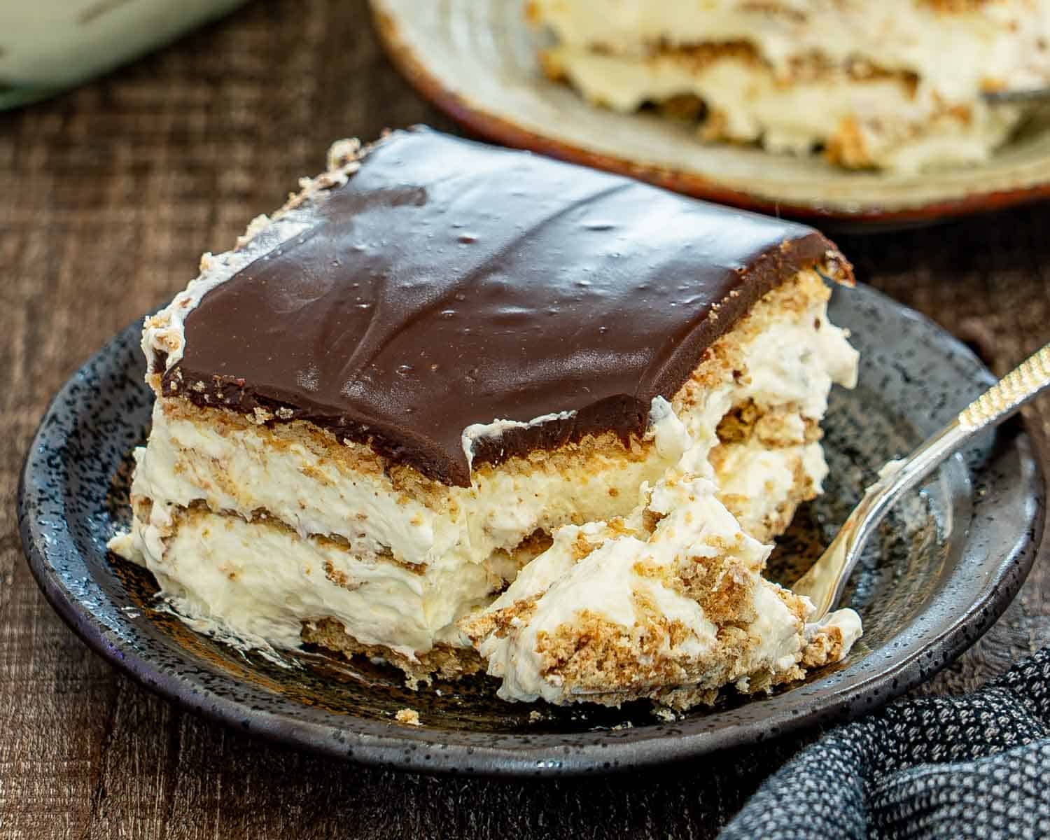 A partially eaten slice of creamy chocolate eclair cake shows soft graham cracker layers beneath glossy chocolate ganache.