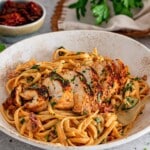 Close view of browned chicken slices on creamy sun-dried tomato linguine, with a fork tucked into the bowl.