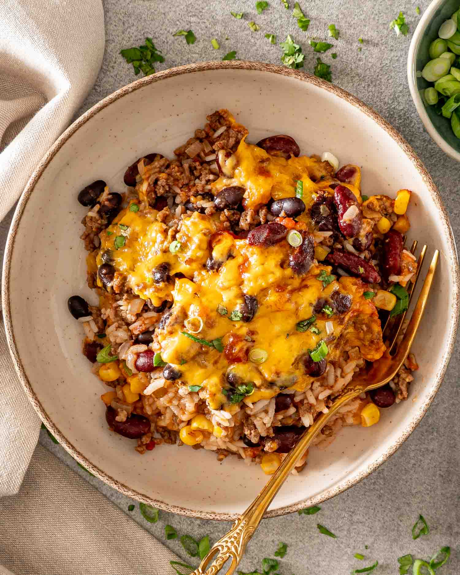 Overhead view of chili rice bake topped with melted cheddar and green onions, served on a plate with a gold fork.