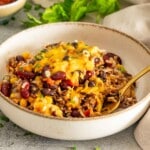 Chili rice bake served in a cream ceramic bowl with melted cheddar, beans, corn, herbs, and a gold fork.