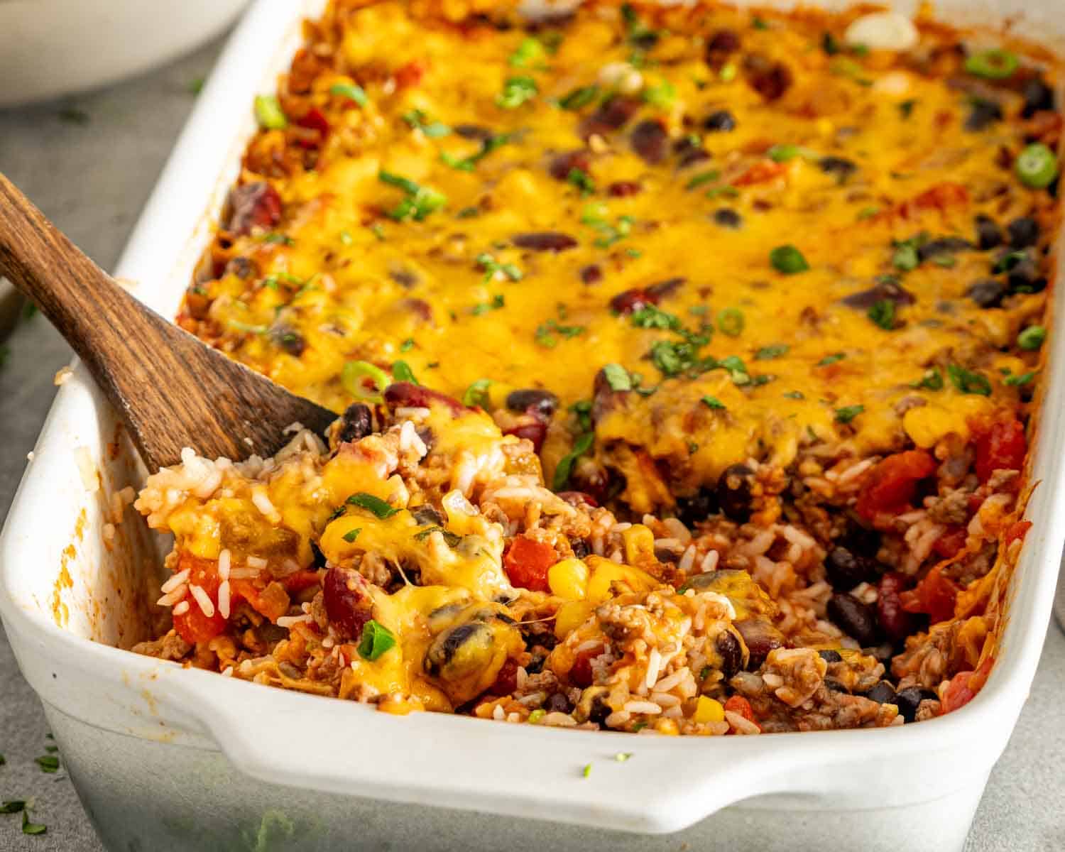 Cheesy chili rice bake in a white baking dish with a wooden spoon holding a serving near the front.