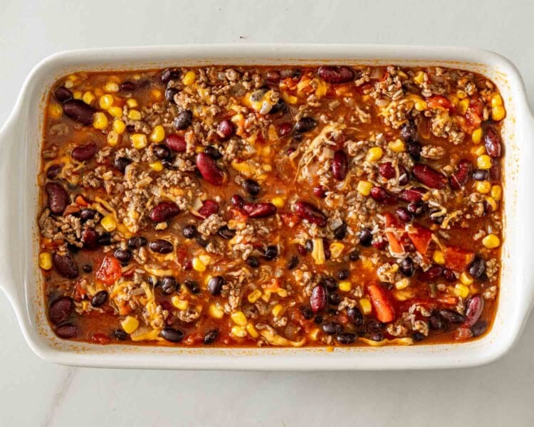 Baked chili rice mixture with ground beef, kidney beans, black beans, corn, tomatoes, and broth in a white dish.